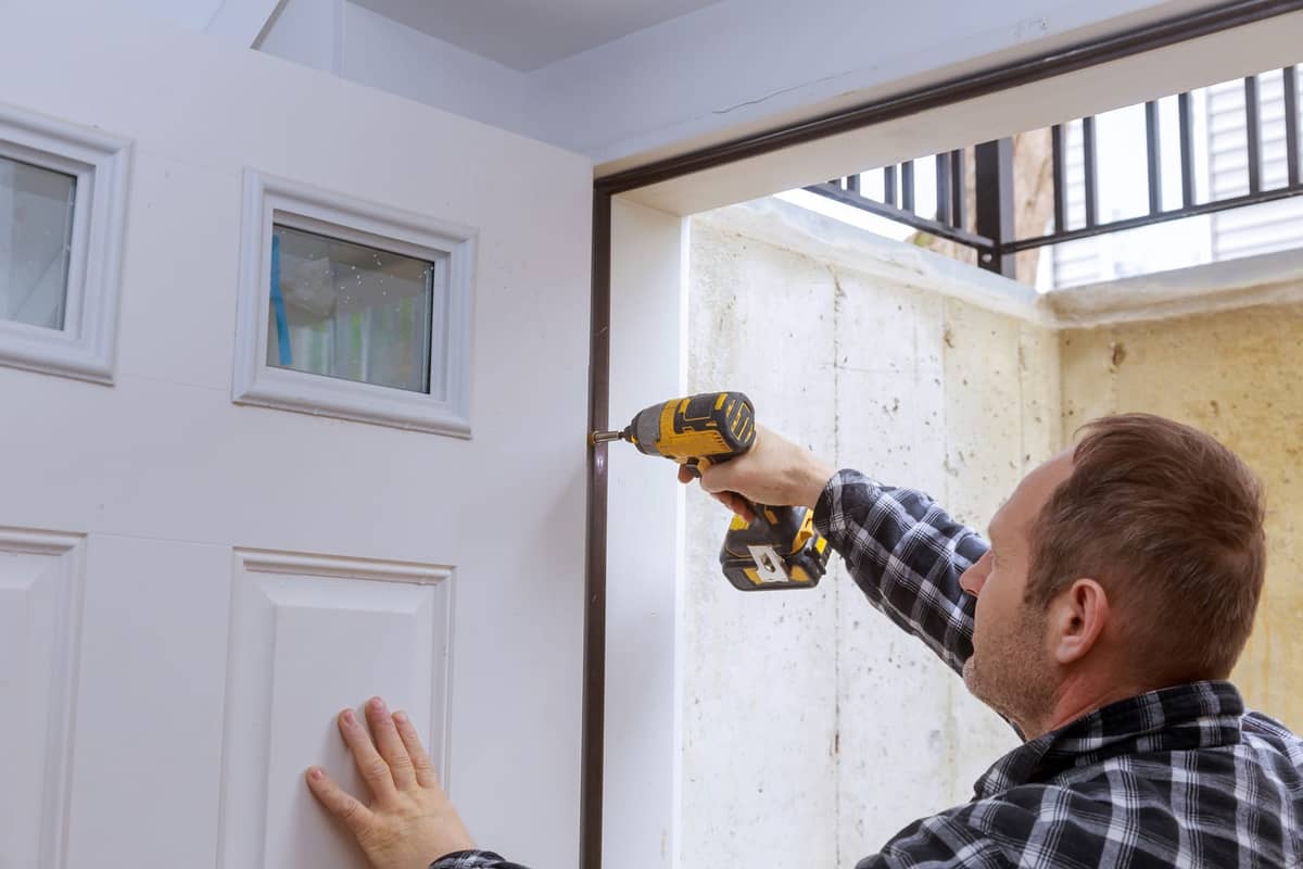A drill driving a screw into a door hinge.