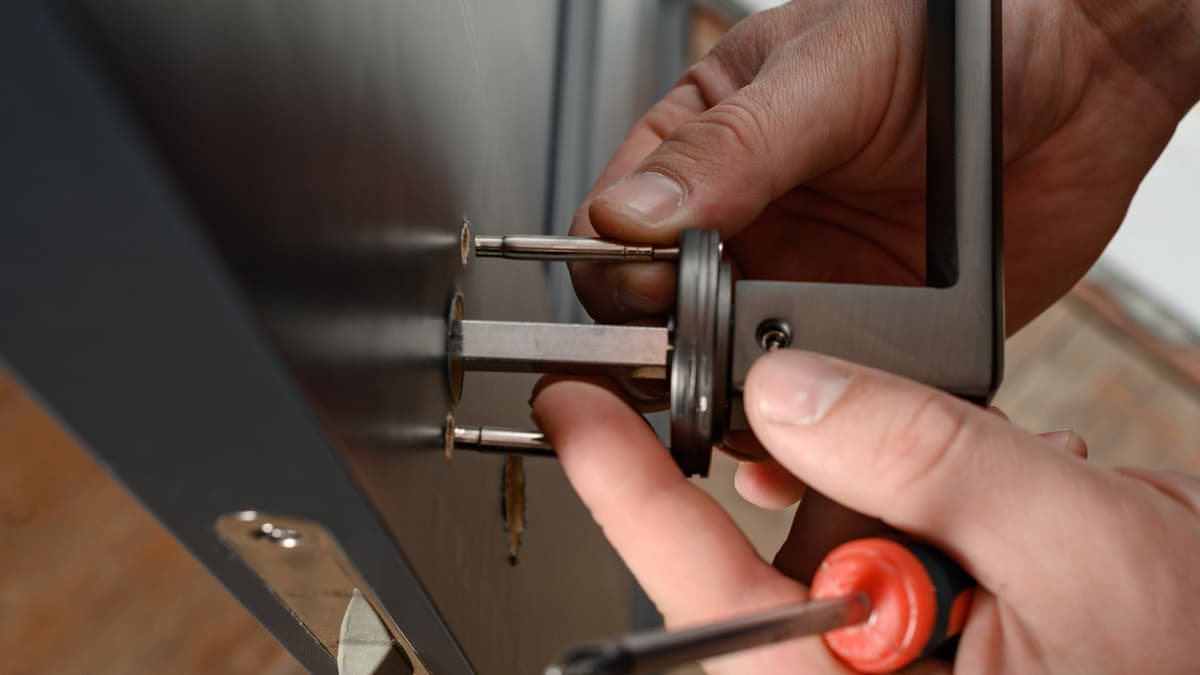 Hands fitting a lock cylinder and latch into a door with a screwdriver.